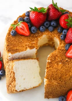 Overhead of angel food cake with a slice taken out of it topped with and surrounded by fresh berries.