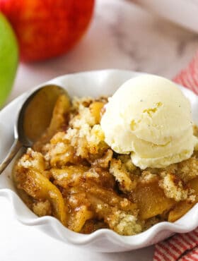 A close-up shot of apple cobbler in a bowl with two apples in the background