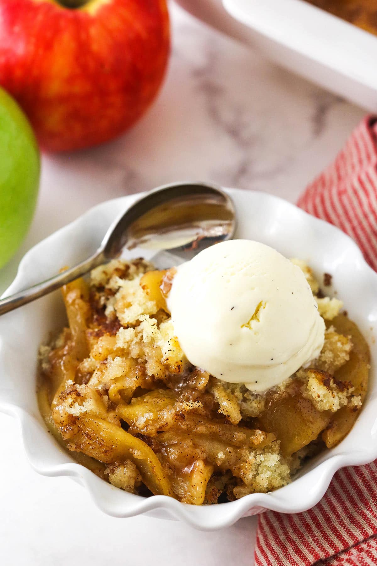 A serving of apple cobbler in a bowl with a spoon and a small scoop of ice cream