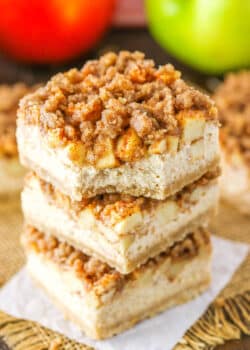An Apple Streusel Cheesecake Bar with a bite removed stacked on top of two more Apple Streusel Cheesecake Bars
