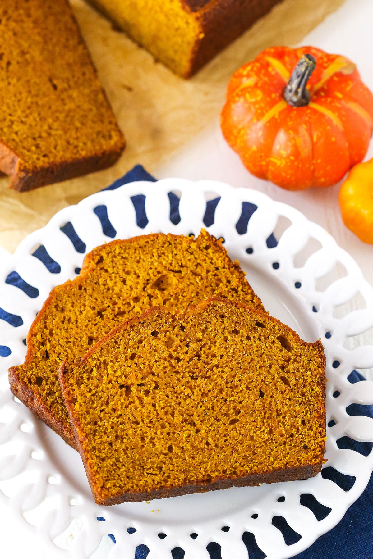 Two slices of Pumpkin Bread on a white plate next to a decorative pumpkin