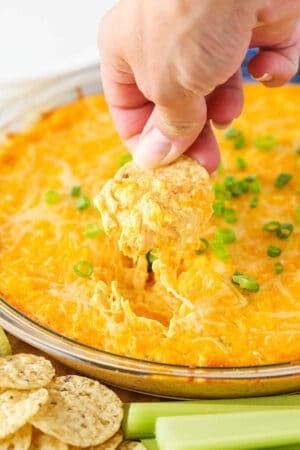 A chip scooping up some Cheesy Buffalo Dip from a clear bowl.