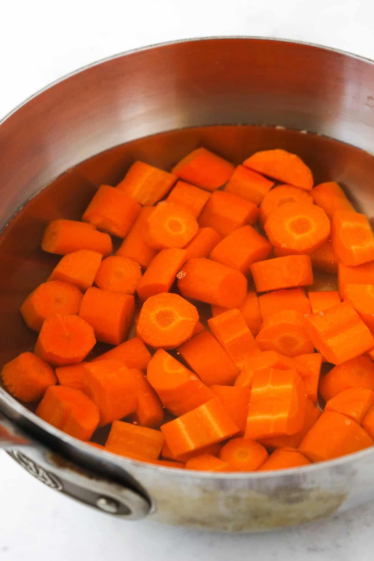 Carrot slices in a large metal bowl with enough water in it to fully submerge them