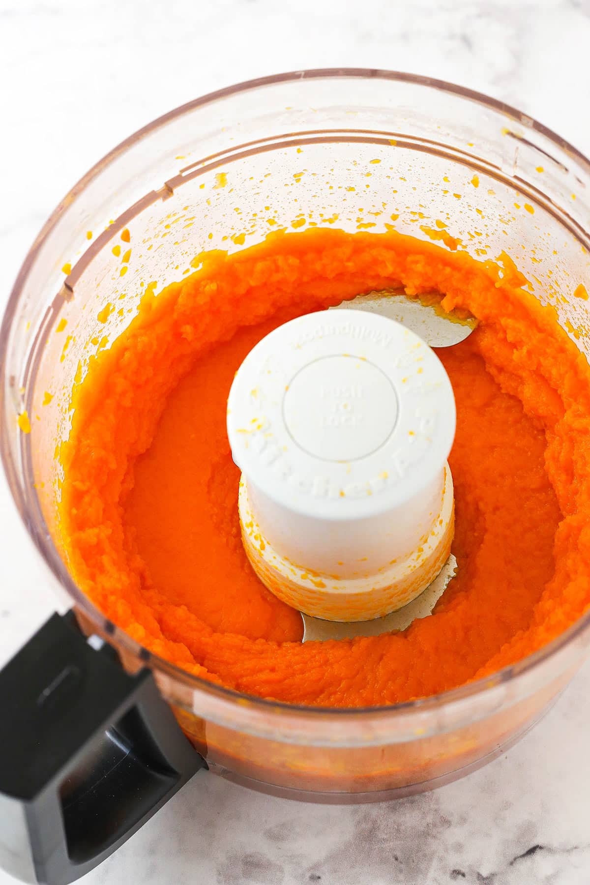 Pureed carrots inside of a food processor sitting on a kitchen countertop
