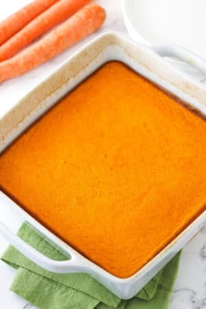 A freshly baked carrot souffle inside of a white baking dish with handles