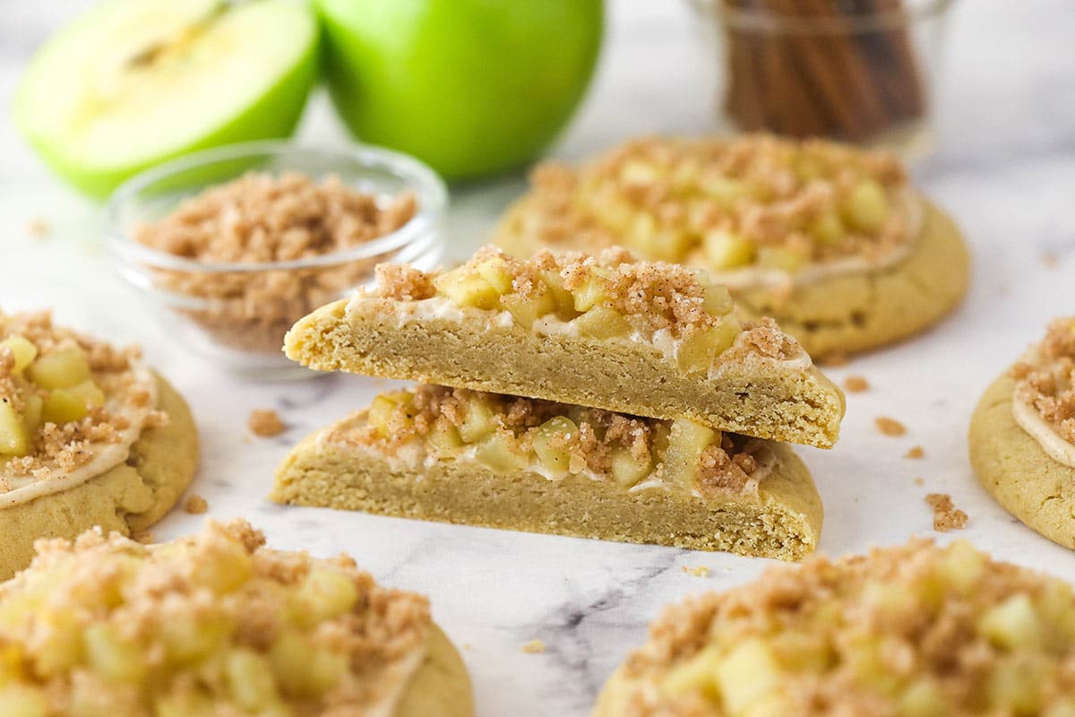 Close up of a Copycat Crumbl Apple Crumb Cake Cookie that is cut in half and surrounded by more cookies.
