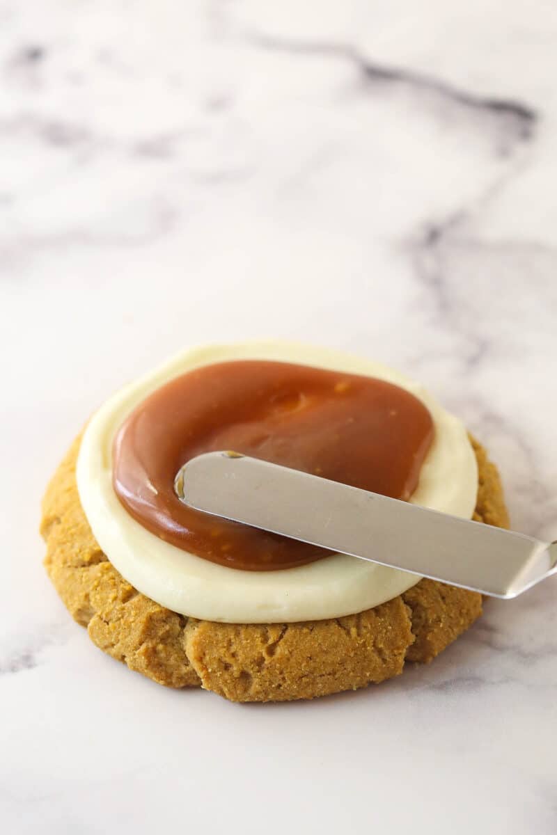 Spreading salted caramel sauce over cheesecake topping on a graham cracker cookie.