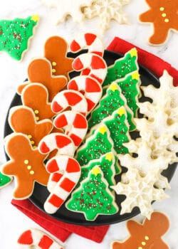 A plate full of neatly organized cut-out sugar cookies with a cloth napkin underneath it
