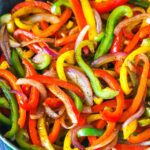 Sliced red yellow and green bell peppers and onions in a skillet
