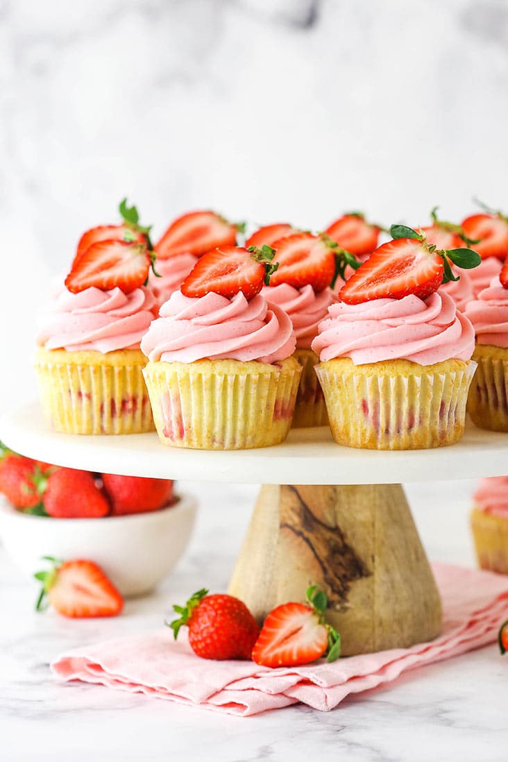 strawberry cupcakes on cake stand with bowl of strawberries in background