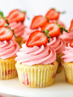 strawberry cupcake on a cake stand with other cupcakes around