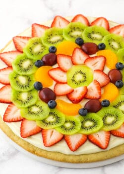 A fully decorated fruit pizza placed on a marble kitchen countertop
