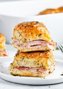 Two ham and cheese sliders stacked on top of one another on a plate