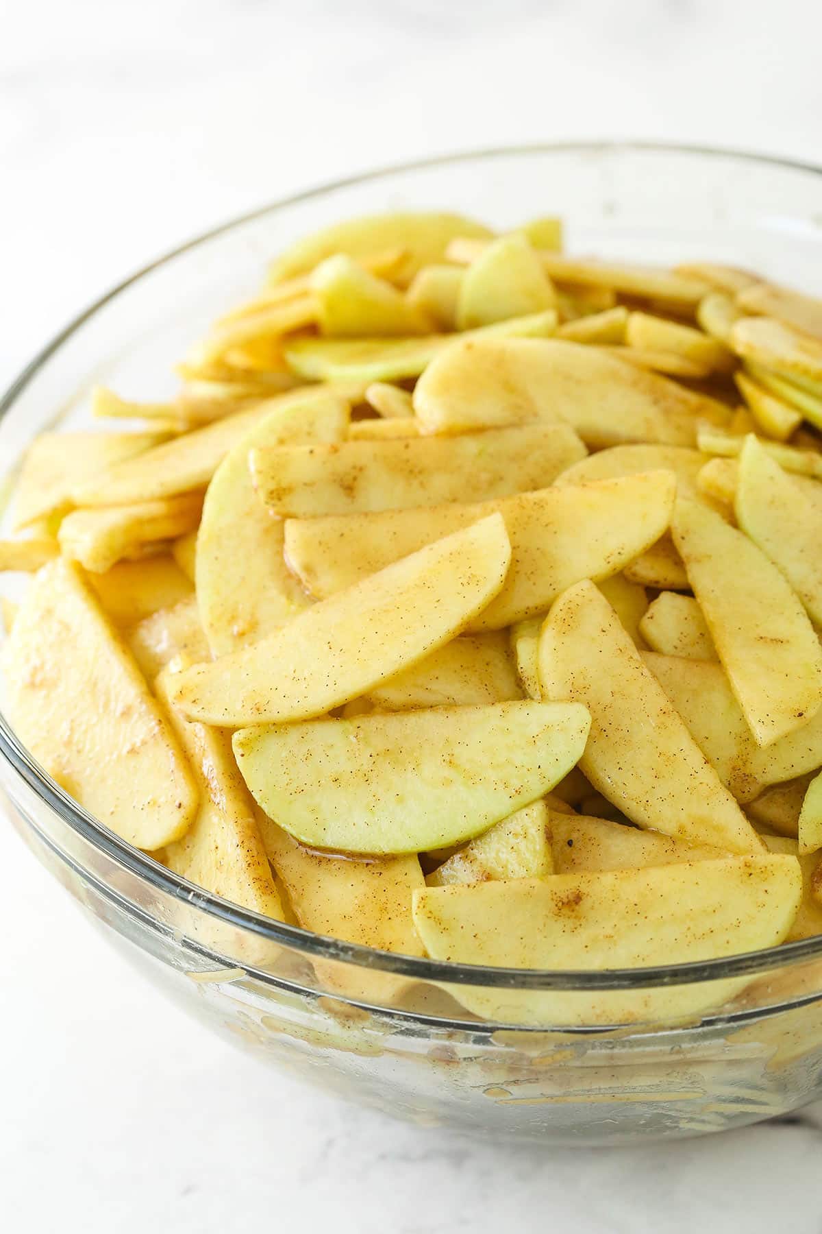 Cut apple slices coated in spices and lemon in a glass bowl.
