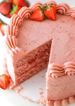 Homemade strawberry cake with a slice taken out of it near fresh strawberries.