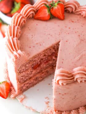 Homemade strawberry cake with a slice taken out of it near fresh strawberries.