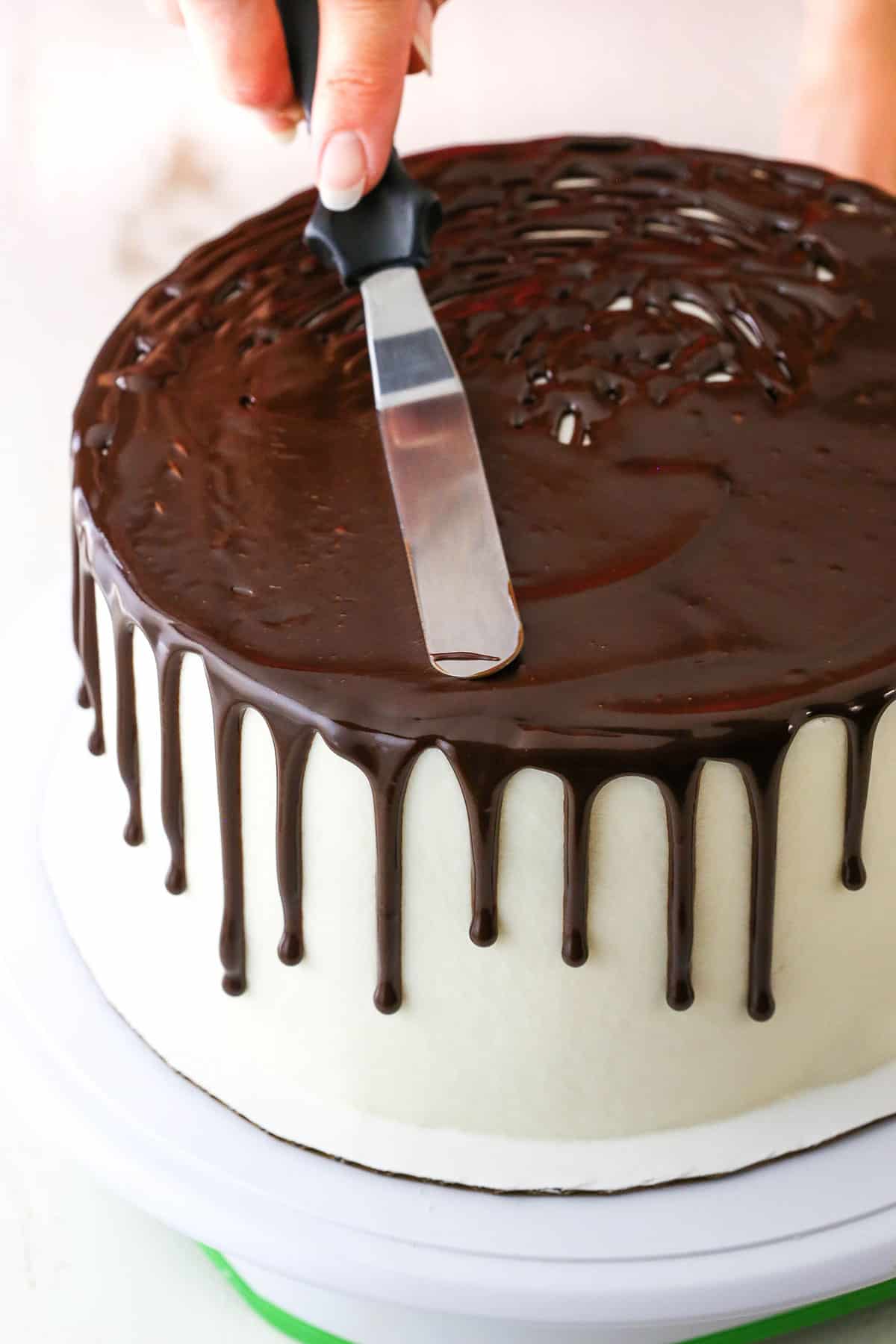How to Make a Chocolate Drip Cake tutorial showing using an offset spatula to smooth the chocolate ganache on top of the cake