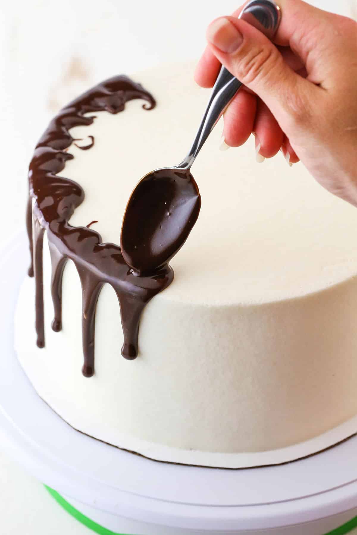 How to Make a Chocolate Drip Cake tutorial showing using a spoon to drip chocolate ganache down the sides of the cake