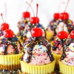 Ice Cream Sundae Mini Cheesecakes topped with chocolate drip and sprinkles with a cherry on top, on a metal platter