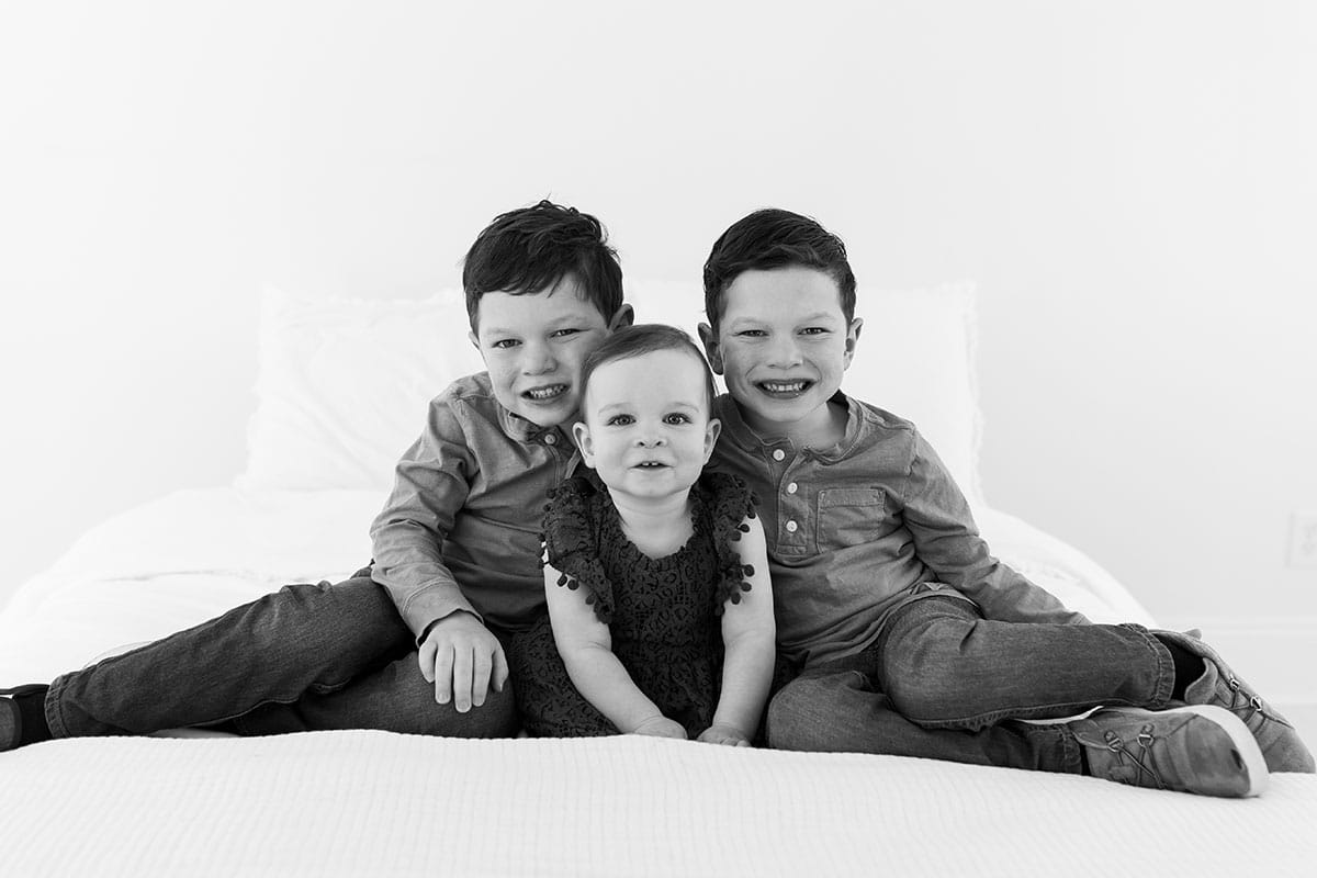 All three kids sitting together on a bed smiling