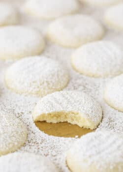 A uniform arrangement of powdered sugar coated vanilla butter cookies with one missing a bite