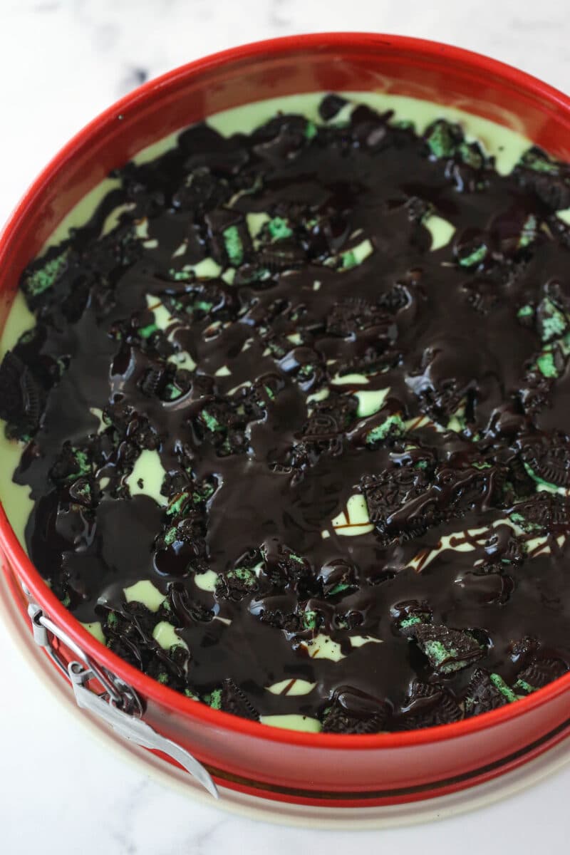 Layering mint Oreo crumbs and chocolate sauce over mint cheesecake filling.