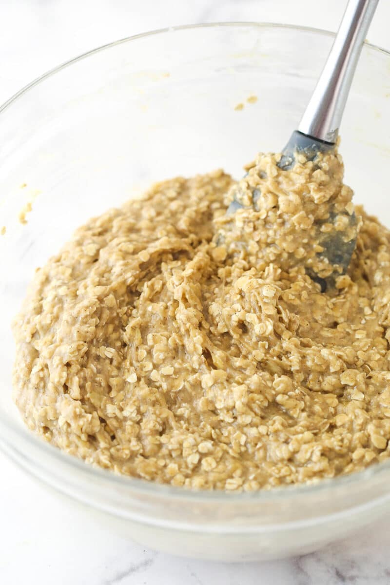 Glass mixing bowl of mixture for Moist Banana Oatmeal Cookies with oats mixed in.
