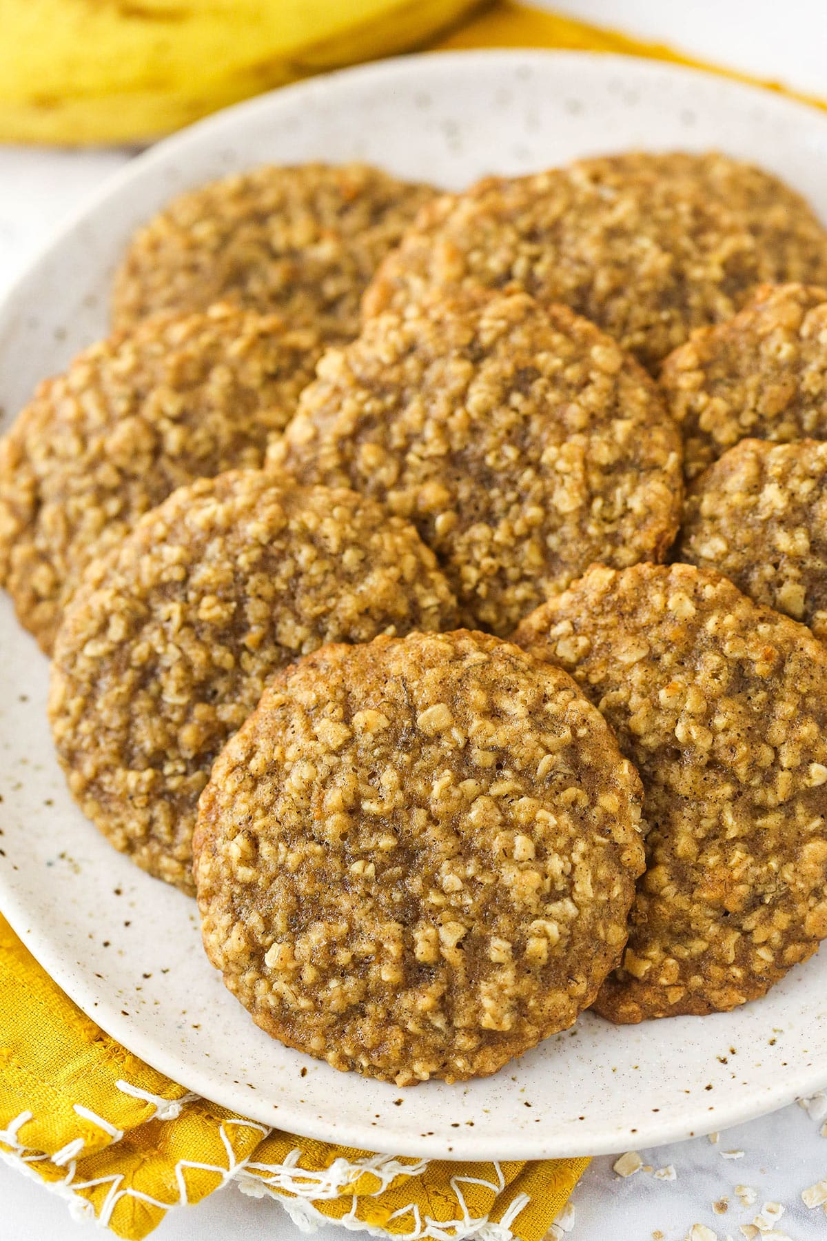 White speckled plate covered with Moist Banana Oatmeal Cookies on top of a yellow napkin.