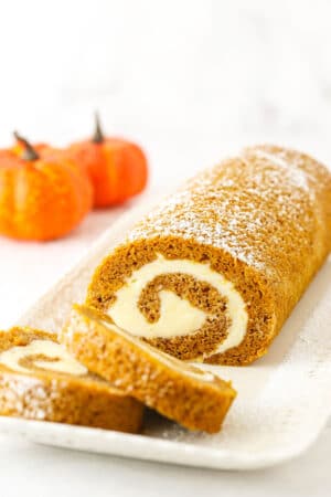 Two slices of Pumpkin Roll Cake layered in front of the rest of the Pumpkin Roll Cake on a white platter