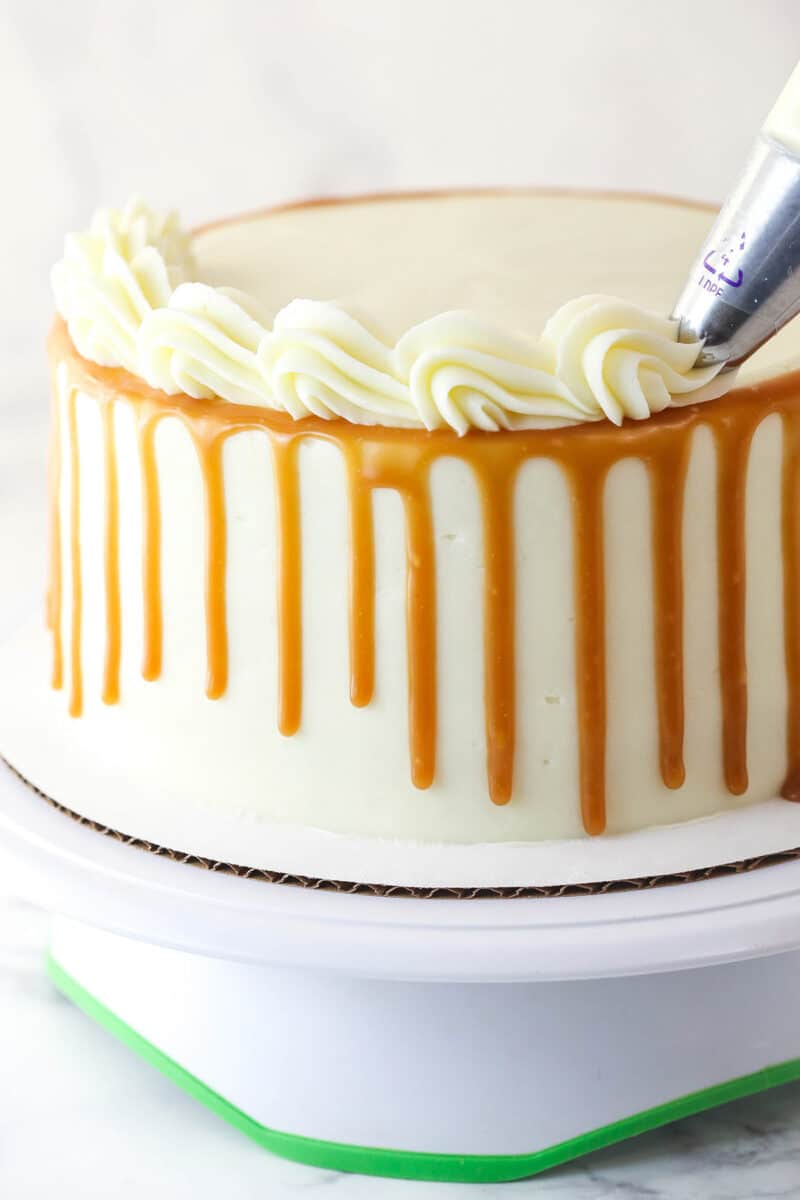 Piping shells of frosting around the top edge of pumpkin layer cake.