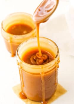 Overhead of dripping Salted Caramel Sauce off a spoon into a clear glass jar