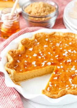 A homemade honey pie in a white pie plate with one slice missing