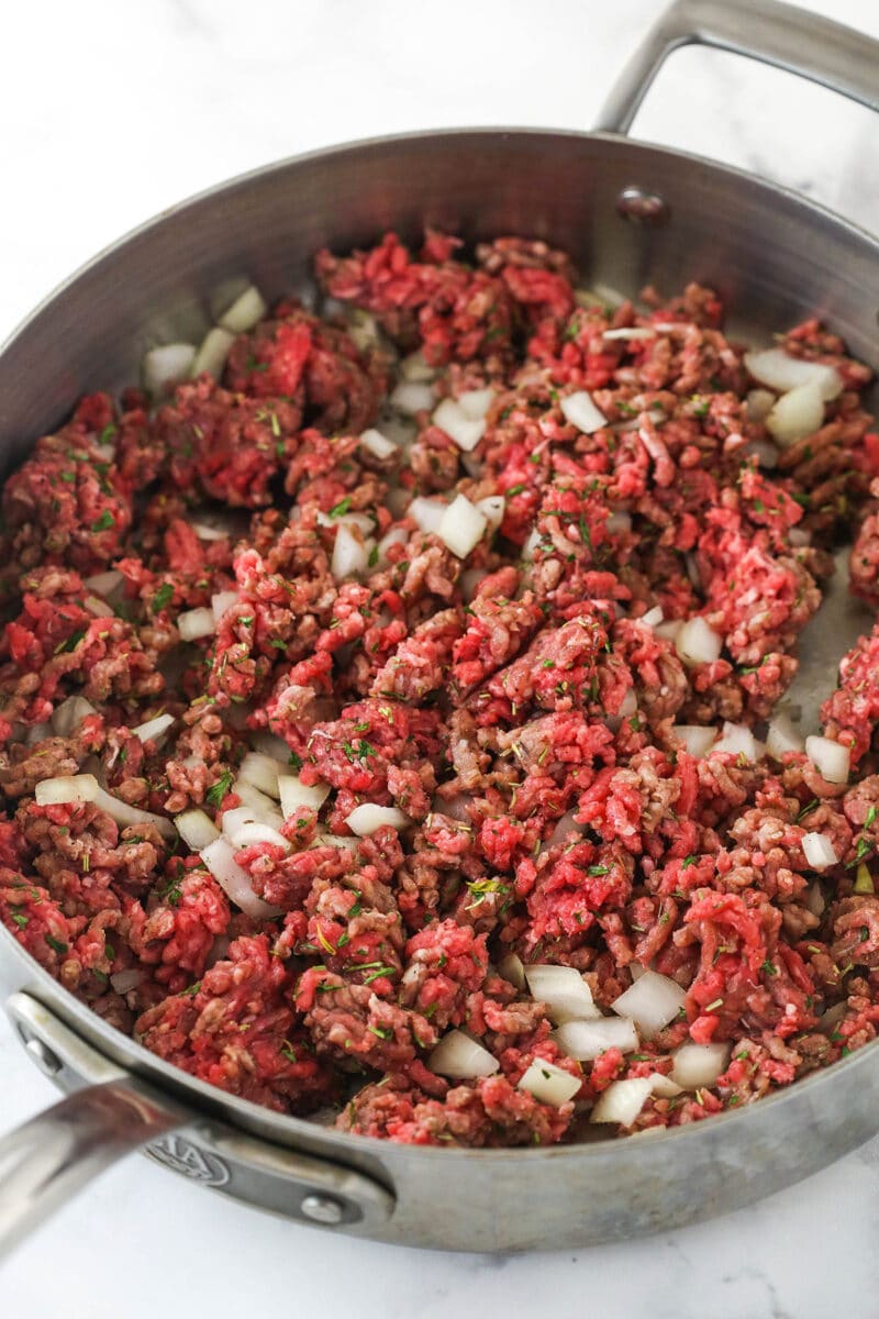 Cooking ground beef and onions with herbs in a pan.