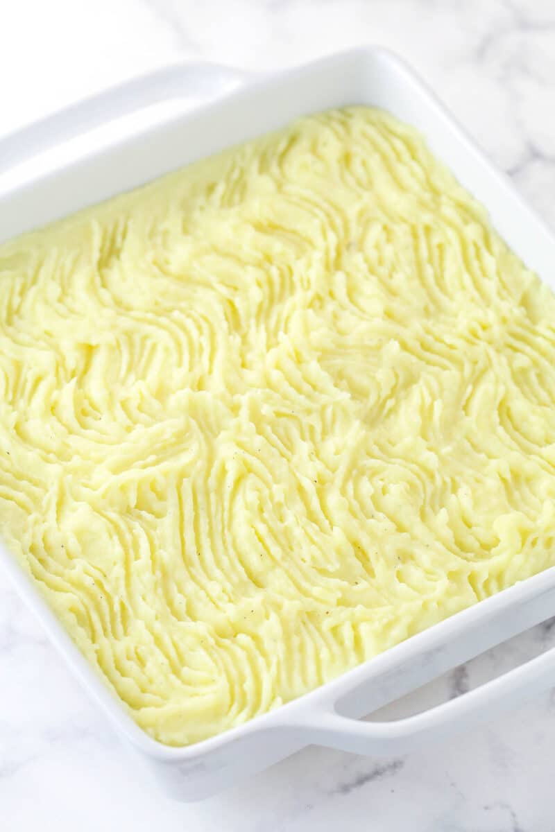 Mashed potatoes spread over meat and vegetable mixture with lines raked through it.