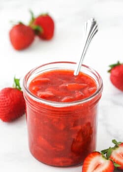 strawberry sauce in a clear jar with strawberries around it