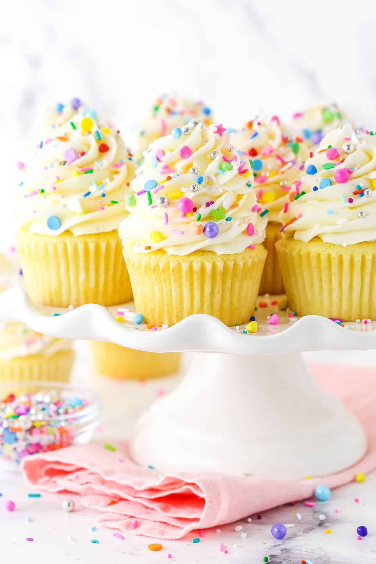 Frosted vanilla cupcakes on a cupcake stand with rainbow sprinkles