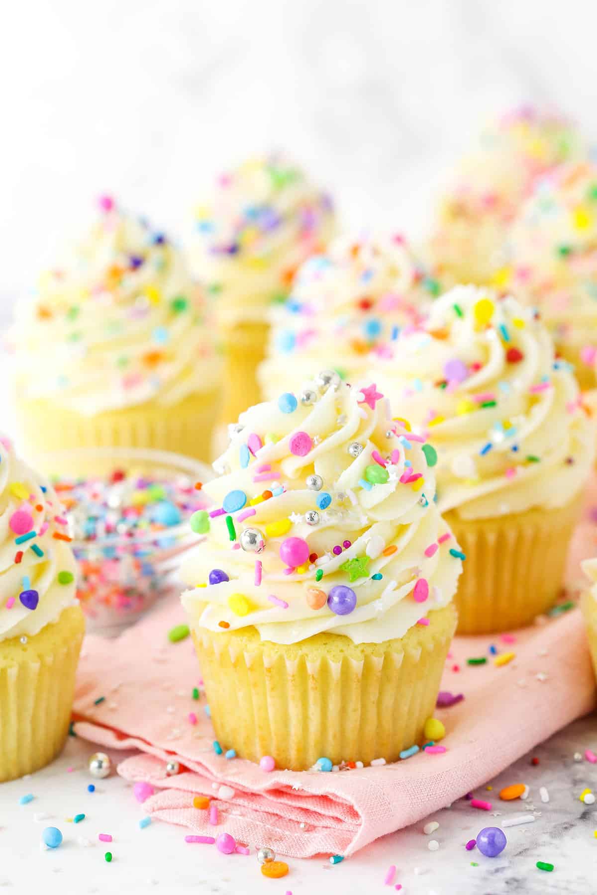 Close up of vanilla cupcakes with vanilla frosting and sprinkles