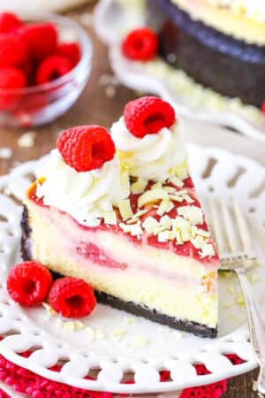 A slice of White Chocolate Raspberry Cheesecake next to a fork on a white plate